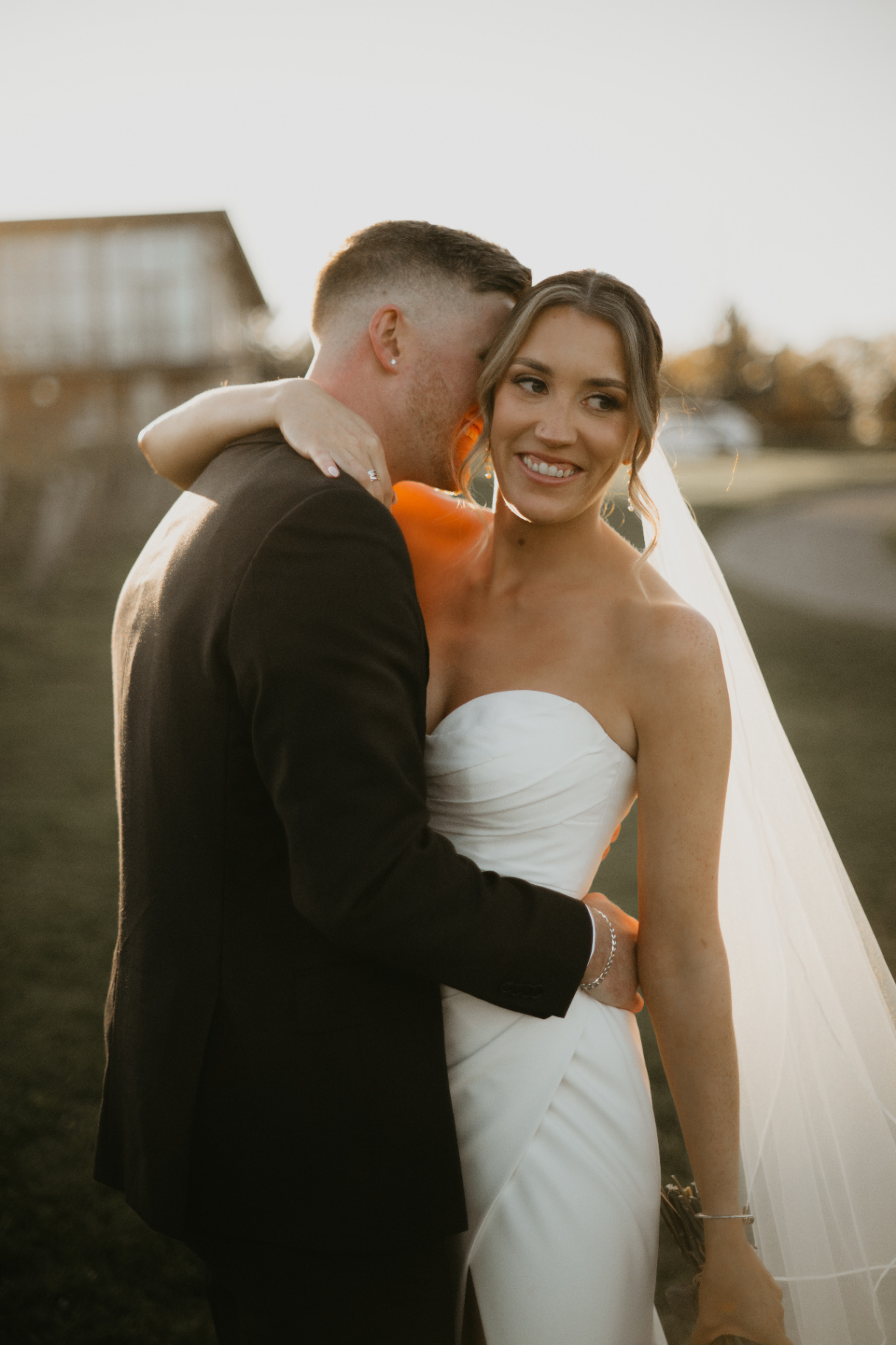 Bride smiling over groom's shoulder in golden light
